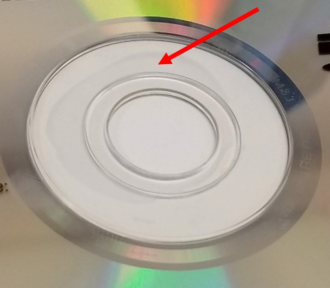 The hub of a DVD movie disc. The arrow points to an area of the hub where the adhesive that glues the DVD structure together is missing. This can lead to separation of disc layers.