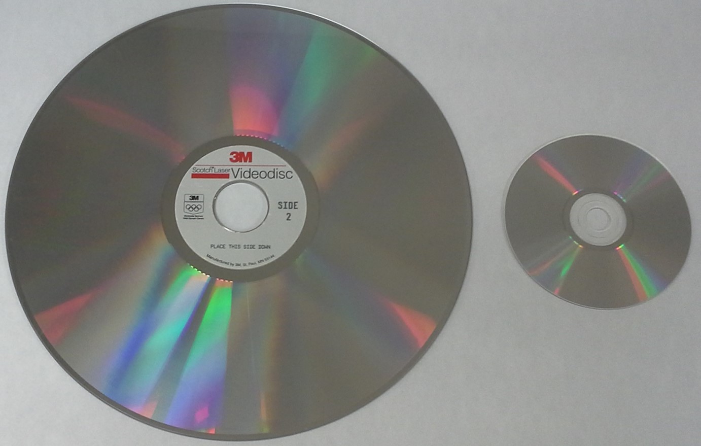 A picture of a 12-inch or 30cm one-sided laserdisc shown next to a standard CD.