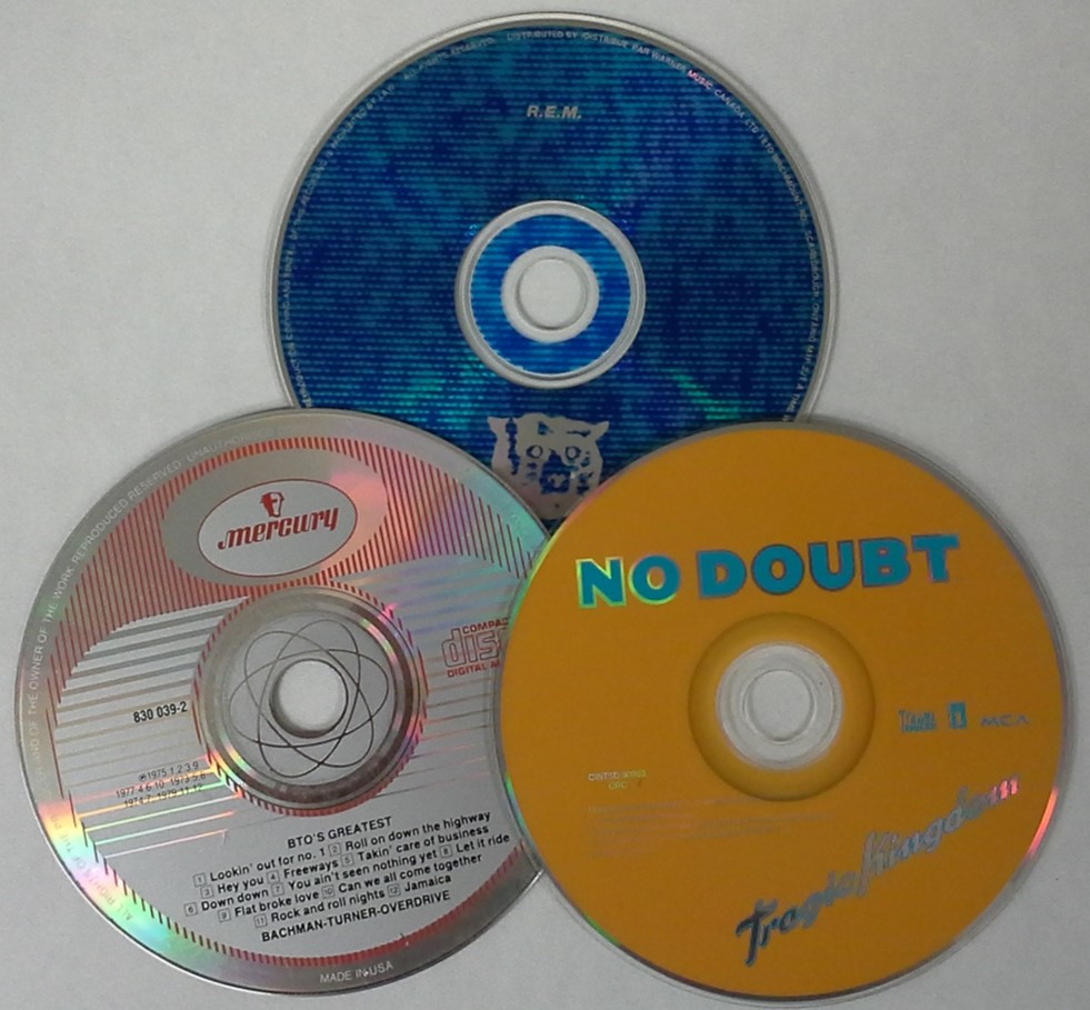 A variety of audio CDs or compact digital audio discs. Shown are CDs from BTO, REM, and No Doubt.