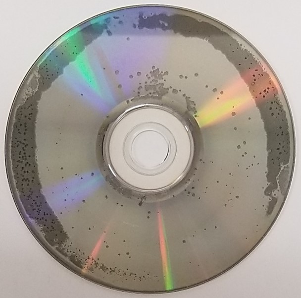 Disc rot or laser rot on a DVD movie disc. Spots of missing metal layer are present as well as discoloration of the metal, especially on the outer portion of the DVD.