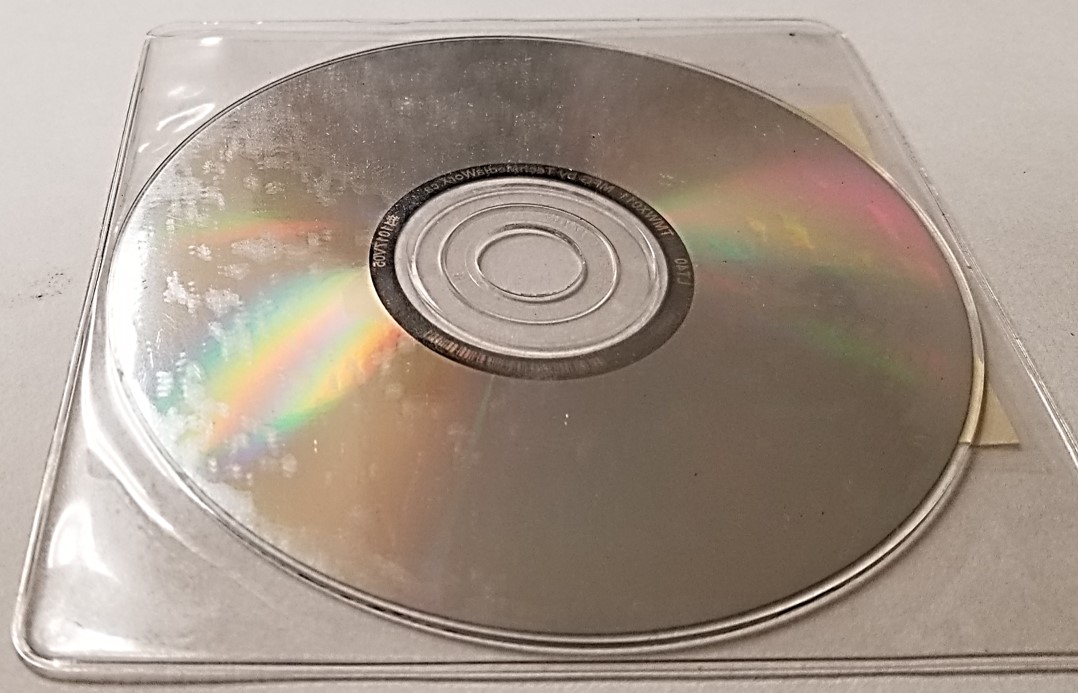 Plastic storage sleeve for CDs, DVDs, or Blu-ray discs that has chemically degraded and left a deposit on the surface of the CD stored inside of it.