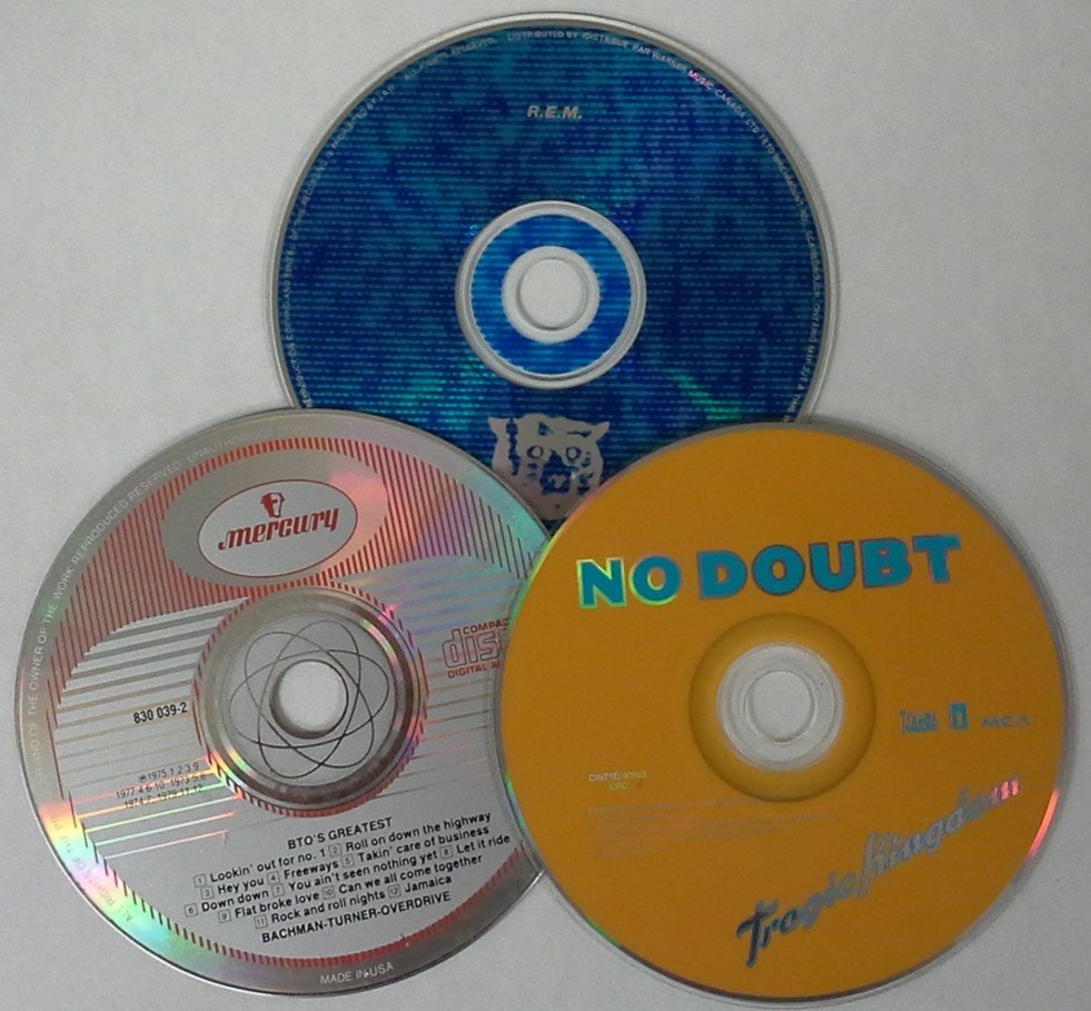 A variety of audio CDs or compact digital audio discs. Shown are CDs from BTO, REM, and No Doubt.